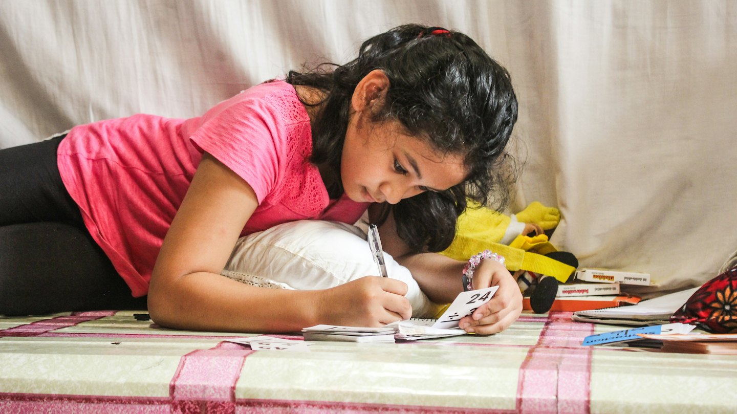 A girl writes in her notebook while solving math problems.