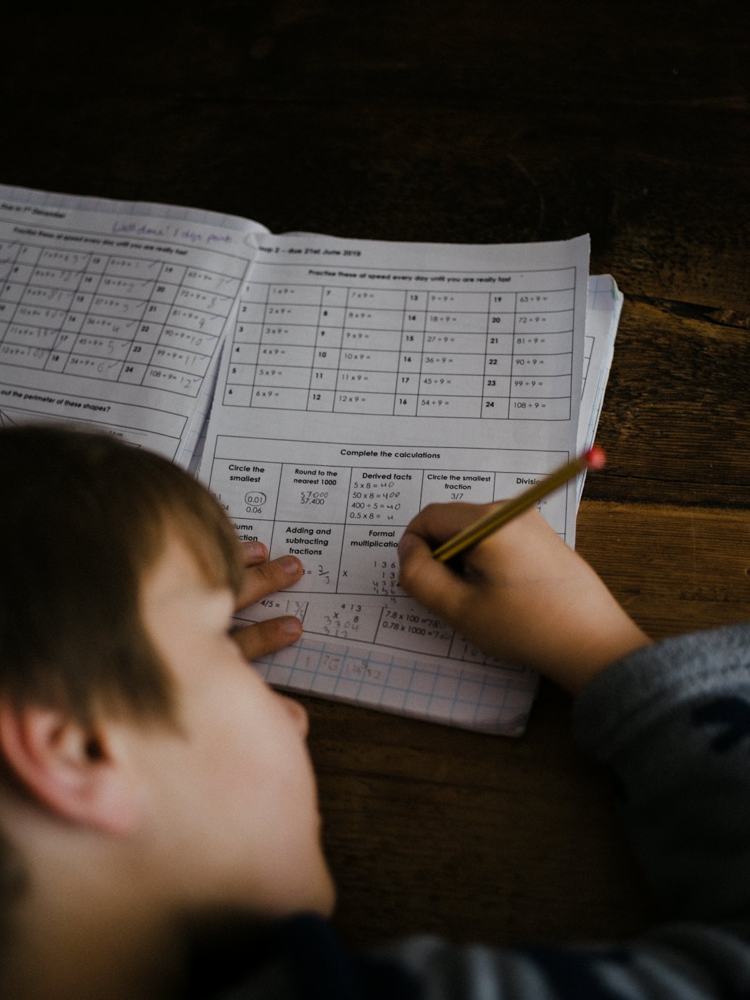 Child's hands holding yellow pencil on math worksheet.